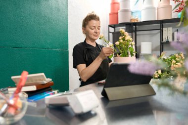 Smiling female florist making flower composition in flower shop. Bouquet of roses in a hat box