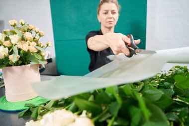 Focused female florist cuts the fabric for a bouquet in a hat box with scissors. Work in a flower boutique