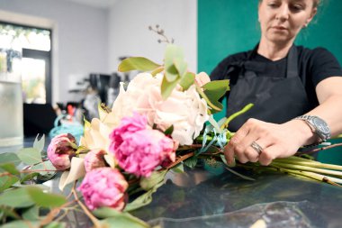 Focused female florist tying luxury bouquet with thin ribbon in flower shop