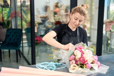 Portrait of a focused female florist at work in a flower shop. Creating chic fashionable flower bouquets