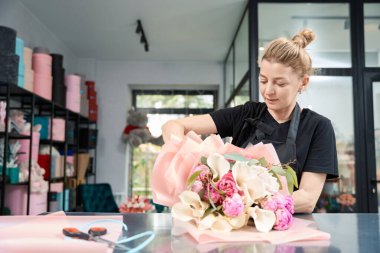 Portrait of a romantic woman in an apron while creating a stylish bouquet of flowers. Florist working in flower shop