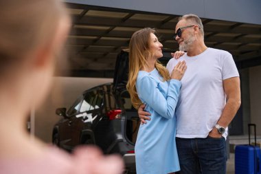 Loving couple embracing look at each other, standing near the new house. Little daughter looks at her parents