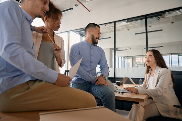 Молодые радостные сотрудники компании разговаривают и улыбаются, находясь в современном офисе со стеклянными стенами