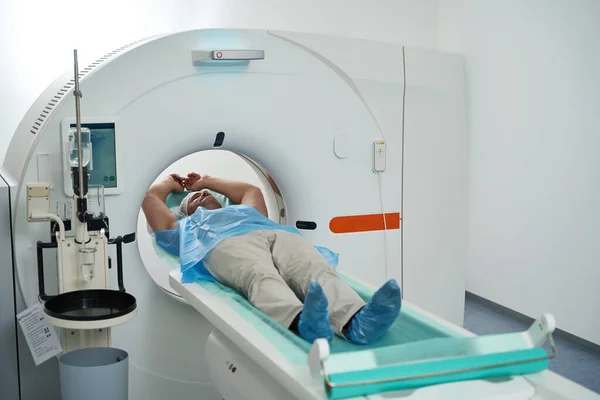 Unshaven patient in a modern medical center lies in the tomograph chamber on a chest diagnostic procedure