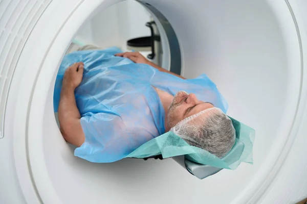 Man in disposable clothes lies in the tomograph chamber for the diagnosis of the abdomen in a modern medical center