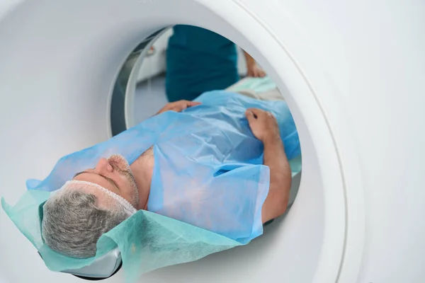 Man in disposable clothes undergoes a procedure of tomography of the abdomen in a modern medical center