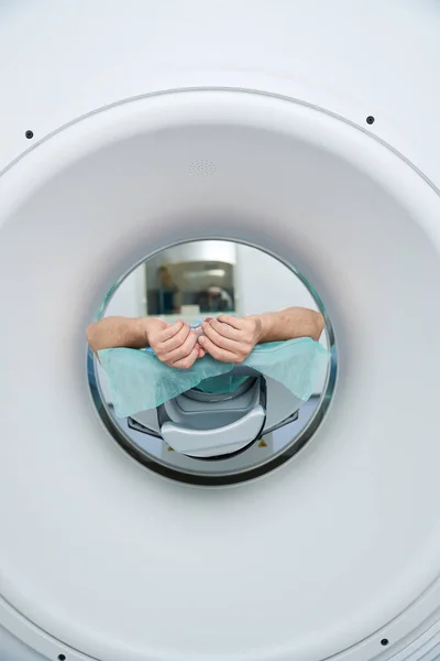 Patient lies in the tomography chamber in the medical center, his hands are raised up