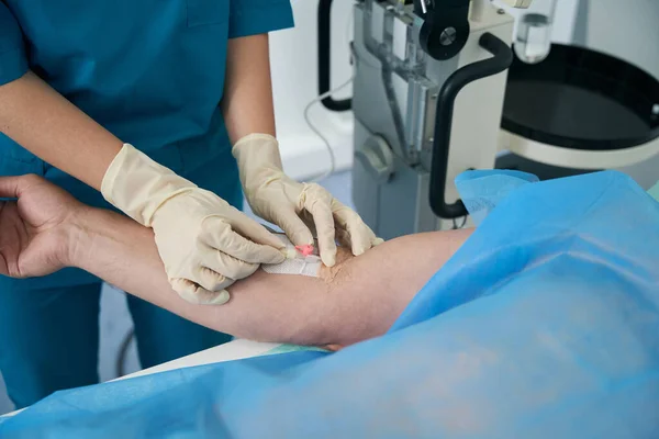 Doctor in medical clothes puts a dropper with medicine to a patient in a manipulation room in a medical center