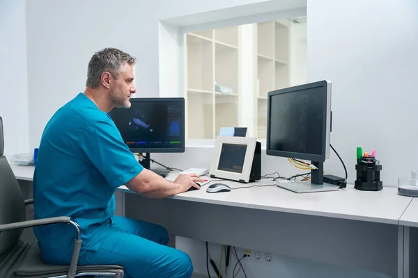 Man in blue medical overalls in a diagnostic center works at a table on a computer