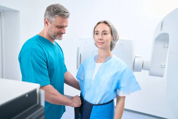 Friendly radiologist in medical clothes puts on a female patient a lead protection for an x-ray procedure