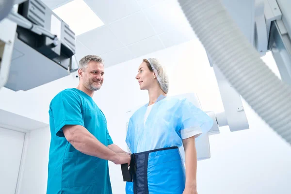 Gray-haired radiologist in a medical center puts on a female patient lead protection before an x-ray procedure on modern machine