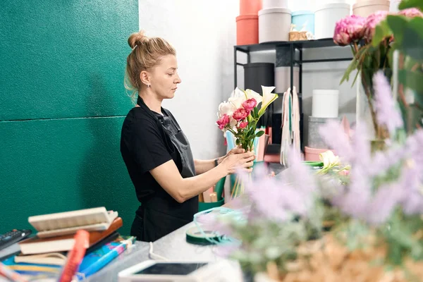 Gentle woman florist admires bouquet of callas, hydrangeas and peonies. Heather stands in foreground