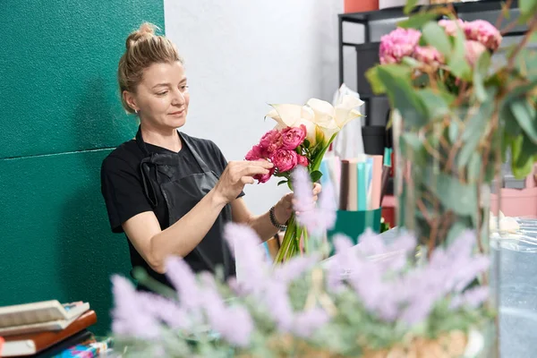 Beautiful woman florist makes up a composition of callas, hydrangeas and peonies. Heather stands in the foreground