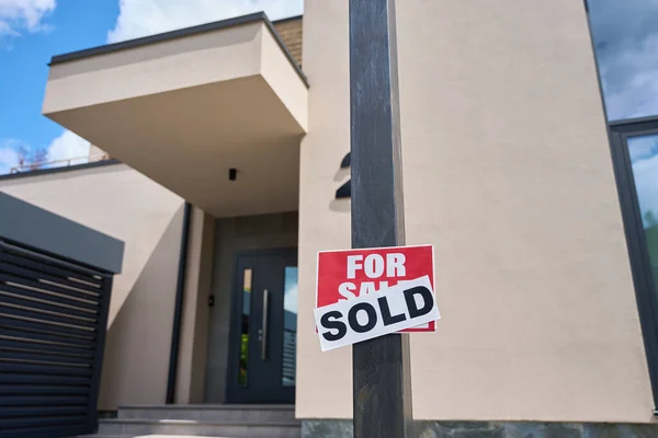 In front of the house there is a sign for sale, with a sticker sold