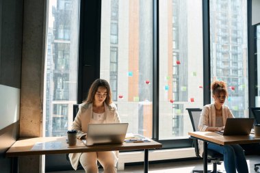 African american women works at notebook in coworking space in front of large window. Girl is sitting next to him