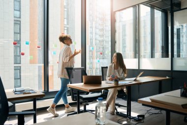 Joyful women employees talking while working in a spacious office with a large panoramic window