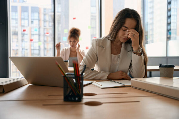 Tired woman sitting at a table with a laptop in the office. Coworking business