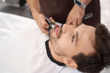 Yüzündeki kılları kesilirken berber koltuğunda uzanmış düşünceli bir adamın yakın plan fotoğrafı.