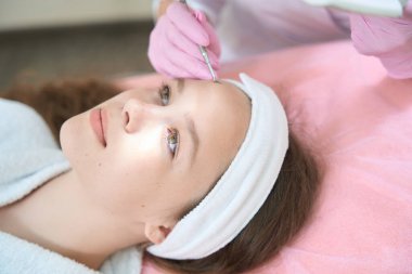 Güzellik muayenehanesinde tek kaşıkla yüzünü temizleyen bir kızın yakın çekimi.