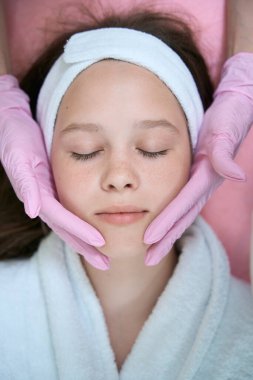 Eldivenli kadın elleri, gözleri kapalı sandalyede yatan bir kızın yüzünü tutuyor. Yukarıdan görüntüle