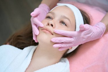 Pembe eldivenli kadın eller güzellik salonundaki kozmetoloji prosedüründen sonra kızların yüzünü inceler.