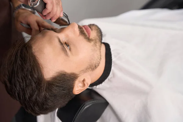 Sereno Morena Homem Deitado Poltrona Barbeiro Tendo Sua Barba Aparada — Fotografia de Stock