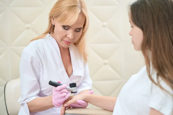 Kadın Dermatolog Güzellik Salonunda Dermatoskoplu Genç Kızın Elini Inceliyor — Stok fotoğraf