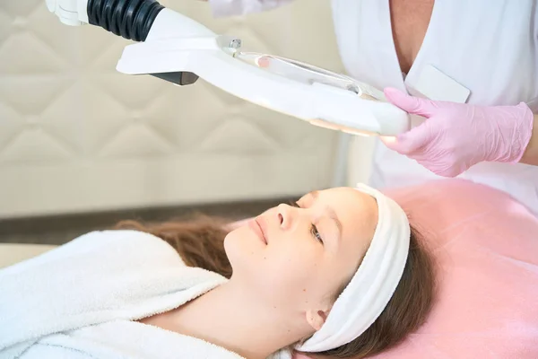 Portrait of a girl lying under a lamp with a magnifying glass in a beauty parlor