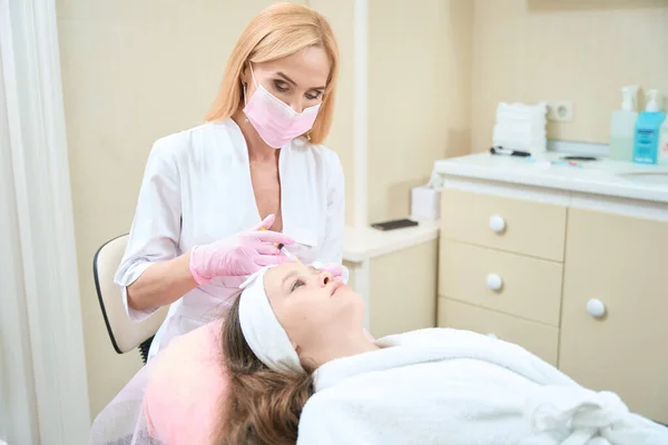 Female cosmetologist in pink mask and gloves makes injection to girl. Acne treatment in the clinic