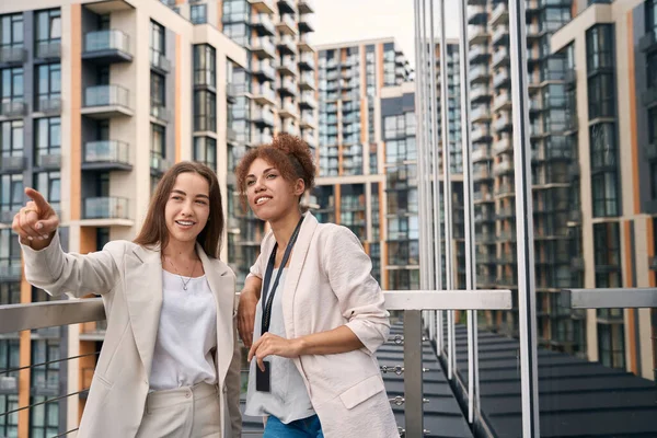 Smiling young corporate employee and her female colleague standing on office balcony