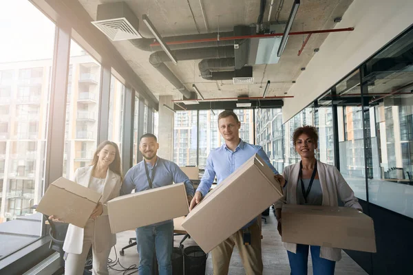 Multiethnic team of company workers holding sealed cardboard boxes in hands and standing in office