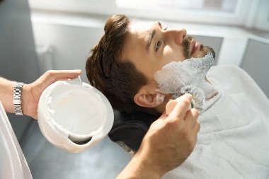 Kuaförde tıraş olmadan önce, yetenekli berber ellerin müşteri yüzünü köpükle kapladığı yakın çekim.