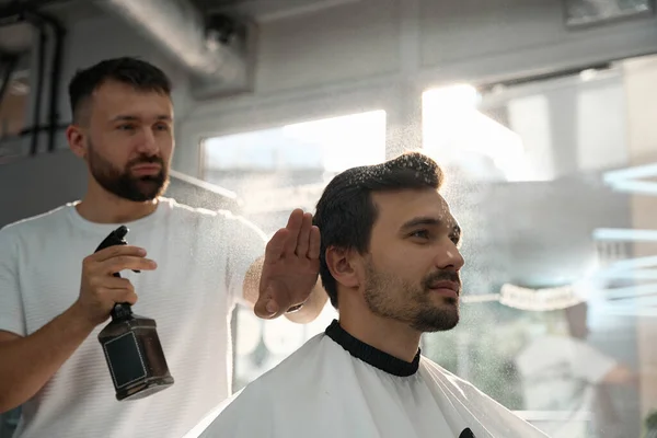 Hair salon employee holding a spray bottle while applying hair product before hair-cutting procedure