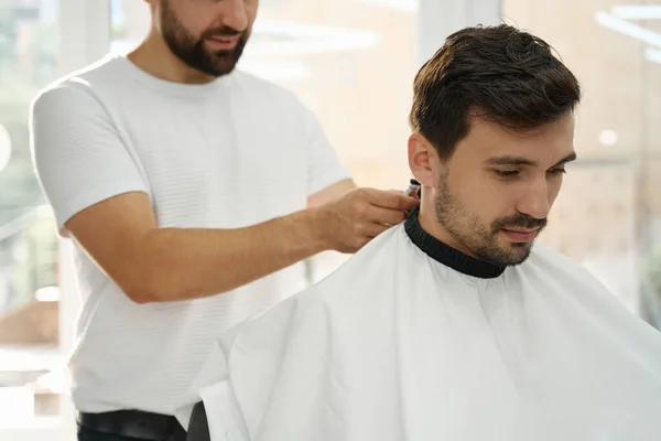 Jovem Calmo Sentado Poltrona Barbearia Enquanto Corta Cabelo Por Cabeleireiro — Fotografia de Stock