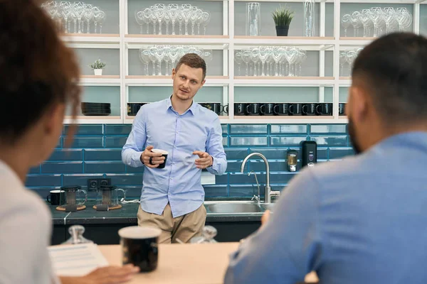 Young company worker talking to his two colleagues seated at bar counter