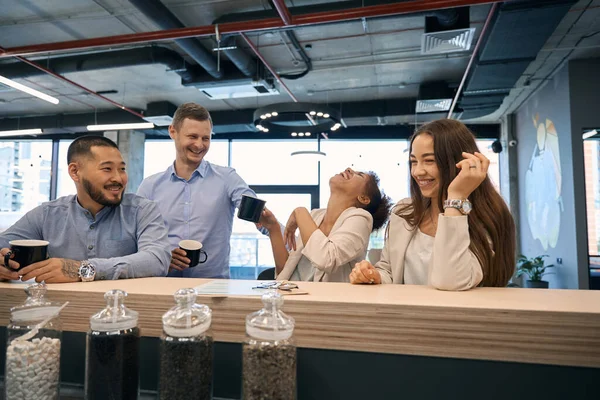Group of cheerful multiracial company employees at bar counter in office kitchen