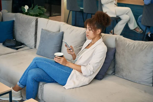 Jovem Focada Sentada Sofá Com Caneca Café Smartphone Nas Mãos — Fotografia de Stock