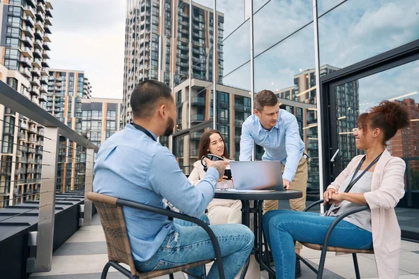 Group of four young company employees holding lunchtime meeting on office balcony