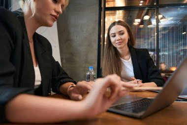 Odaklanmış şirket çalışanı ofis masasında oturuyor ve iş arkadaşına dizüstü bilgisayar ekranını gösteriyor.