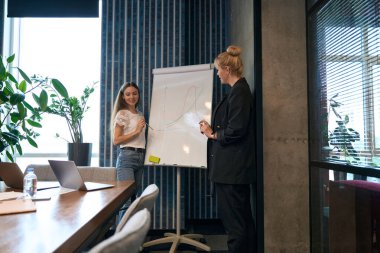 Gülümseyen kadın ofis çalışanı meslektaşıyla birlikte tahtada dururken dizüstü bilgisayara bakıyor.