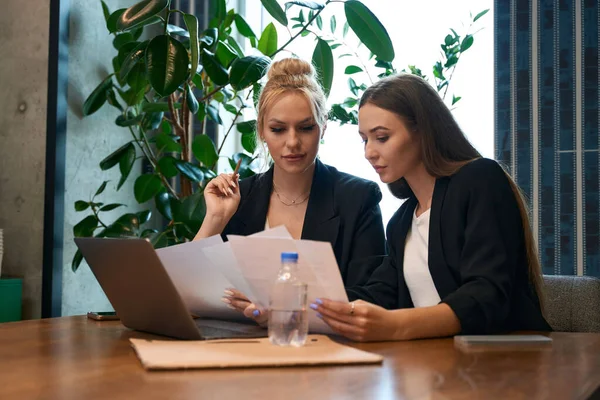 Focused young company workers sitting at office desk and looking through documents