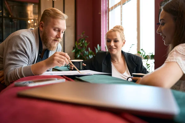 Odaklanmış işadamı, gülümseyen bayan meslektaşlarına elinde kalemle belgeyi işaret ediyor.
