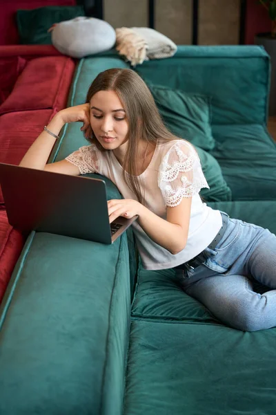 일하는 공간에서 소파에 앉아서 휴대용 컴퓨터를 사용하는 집중력의 아가씨 — 스톡 사진
