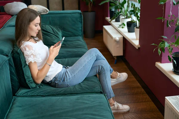 Vista Lateral Una Joven Concentrada Sentada Cómodo Sofá Con Smartphone — Foto de Stock