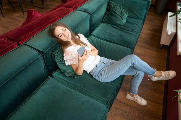Sorrindo Alegre Jovem Deitada Sofá Confortável Olhando Para Celular Suas — Fotografia de Stock