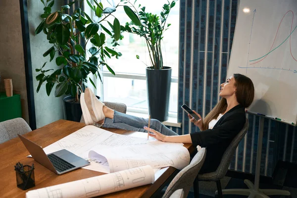 夢のような絵を描く女性と鉛筆とスマートフォンはオフィスの机の上に足で椅子に座って — ストック写真