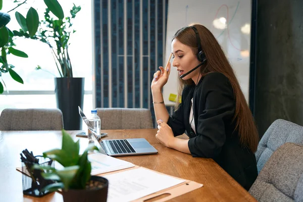 Side view of online store employee in headset sitting at office desk and talking to customer