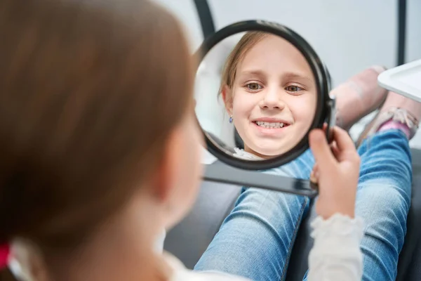 Konzentrierte Kleine Patientin Sitzt Zahnarztstuhl Und Blickt Handspiegel Auf Ihren — Stockfoto