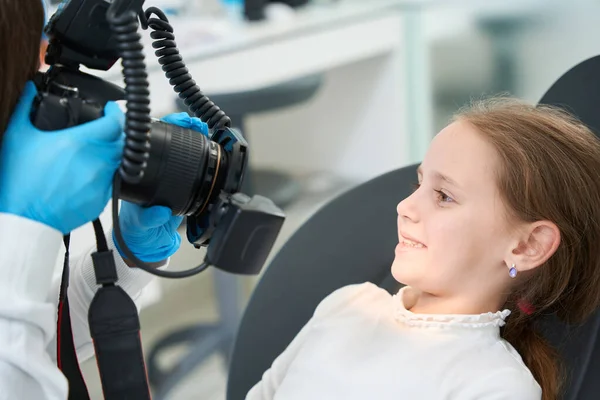 Stomatolog Trzymający Aparat Cyfrowy Przed Uśmiechniętym Dzieckiem Siedzącym Krześle Dentystycznym — Zdjęcie stockowe