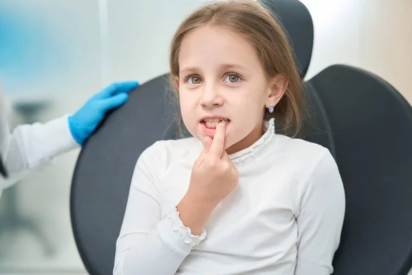 坐在牙医办公室里的十几岁以下的女孩指着嘴里有问题的牙齿 — 图库照片